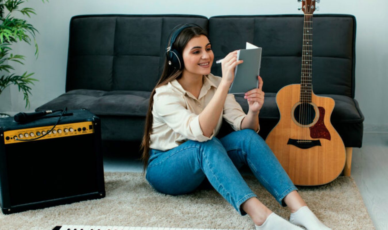 smiley-female-musician-writing-songs-notepad-acoustic-guitar-keyboard